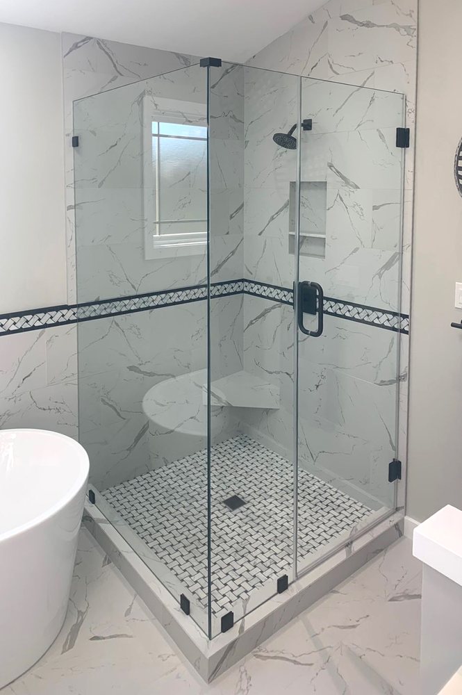 Frameless corner shower with clear glass and matte black hinges next to a freestanding tub