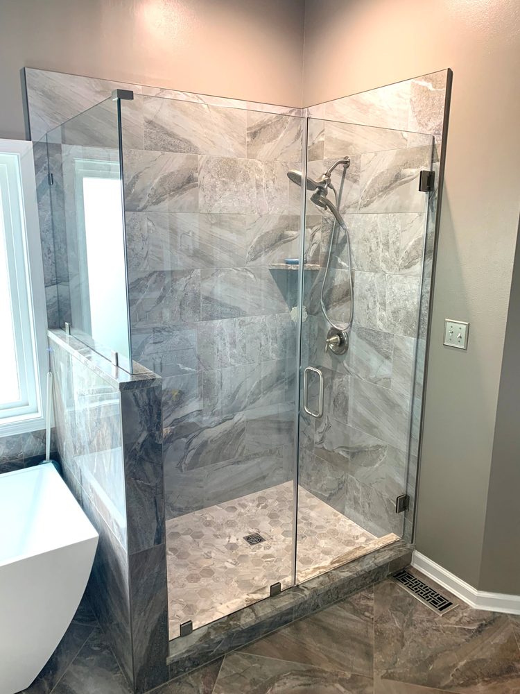 Frameless corner glass enclosure on a tiled half wall with brushed nickel hinges and handle