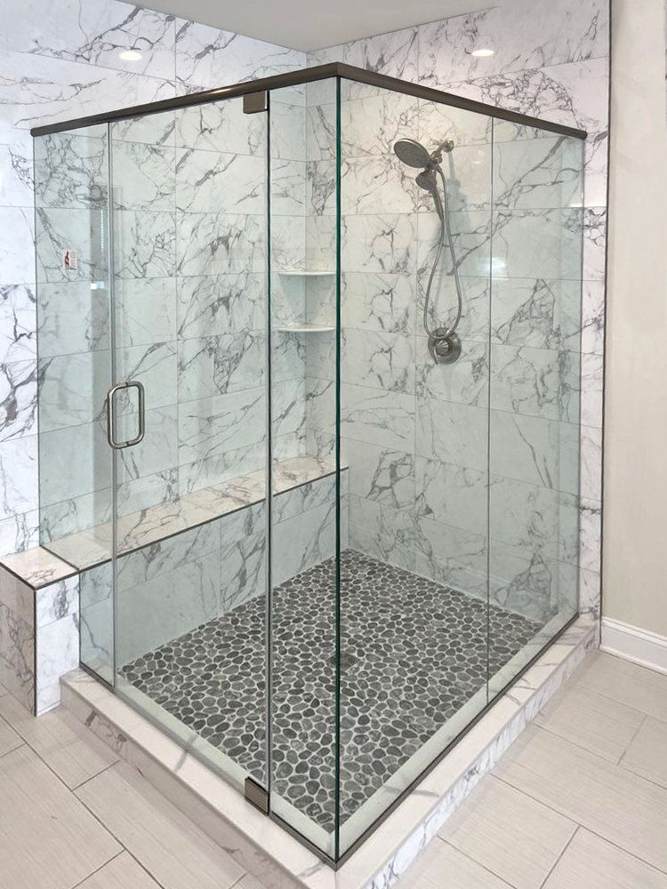 Frameless corner shower with marble-look tile walls and a pebble floor
