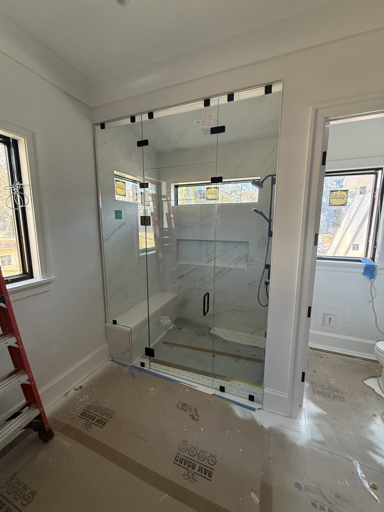 Full-height frameless glass enclosure with matte black clamps and hinges in a new build