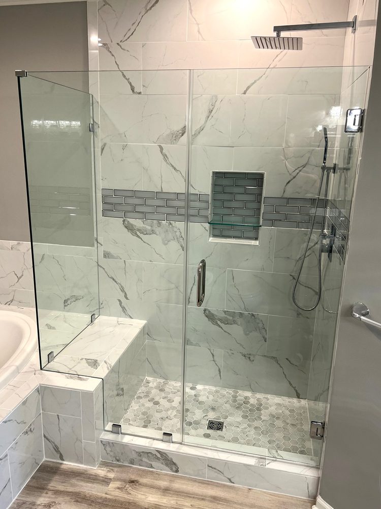 Frameless glass door and panels over a tiled bench in a marble-look shower with a rain head