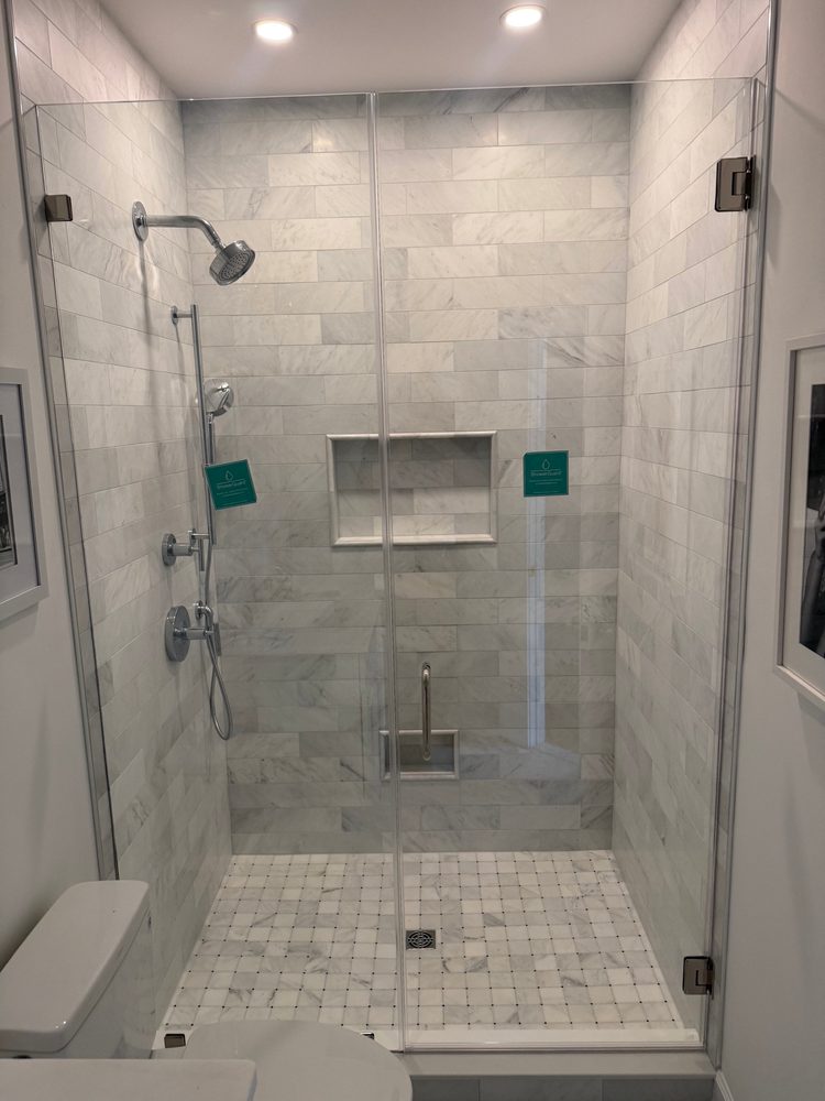 Frameless glass door and panel on a marble-tile shower with a basketweave floor