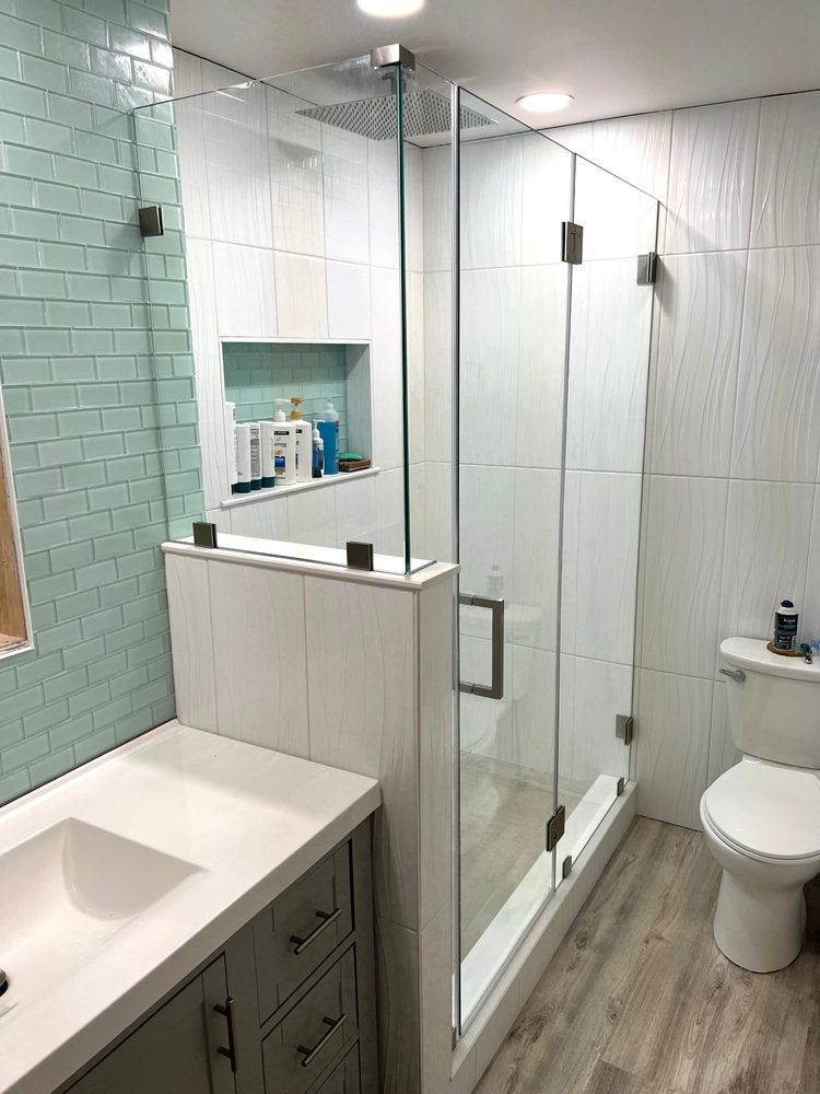 Frameless glass enclosure on a half wall with a brushed nickel header and hinges, next to a vanity
