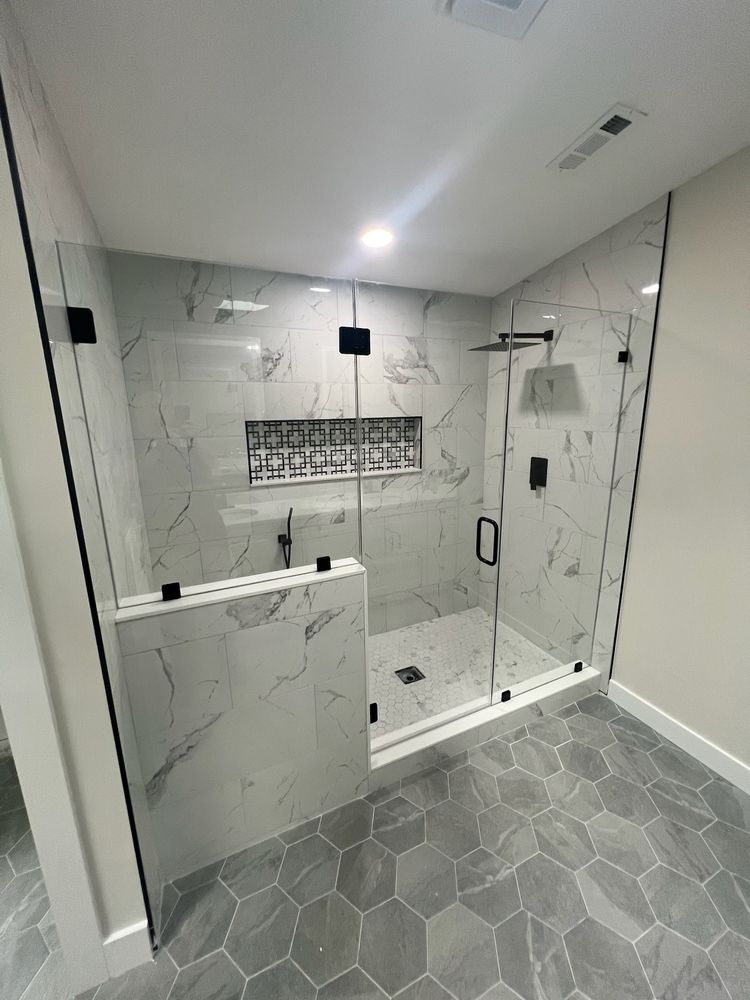 Frameless glass shower enclosure sitting on a tile knee wall, gray hexagon floor tile