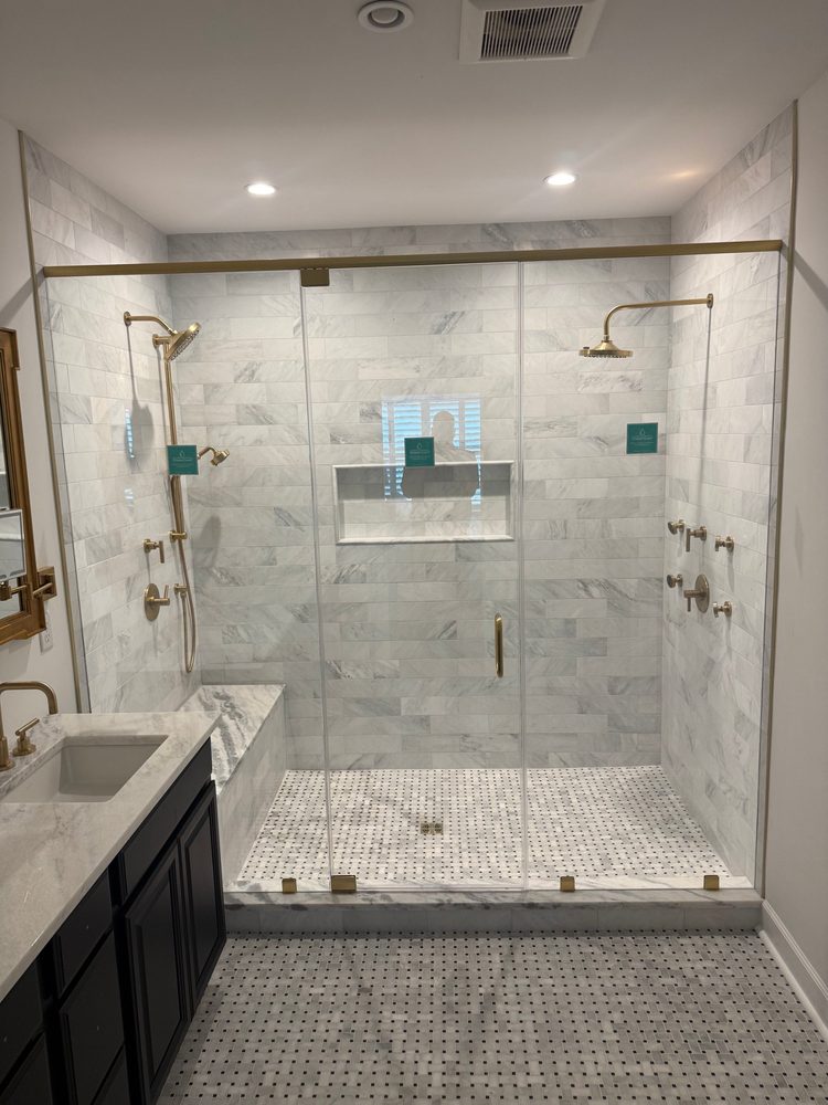 Wide frameless glass enclosure with brushed brass header and hardware around a marble double shower