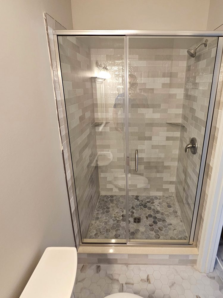 Hinged glass shower door and panel with a brushed nickel frame on a tiled curb
