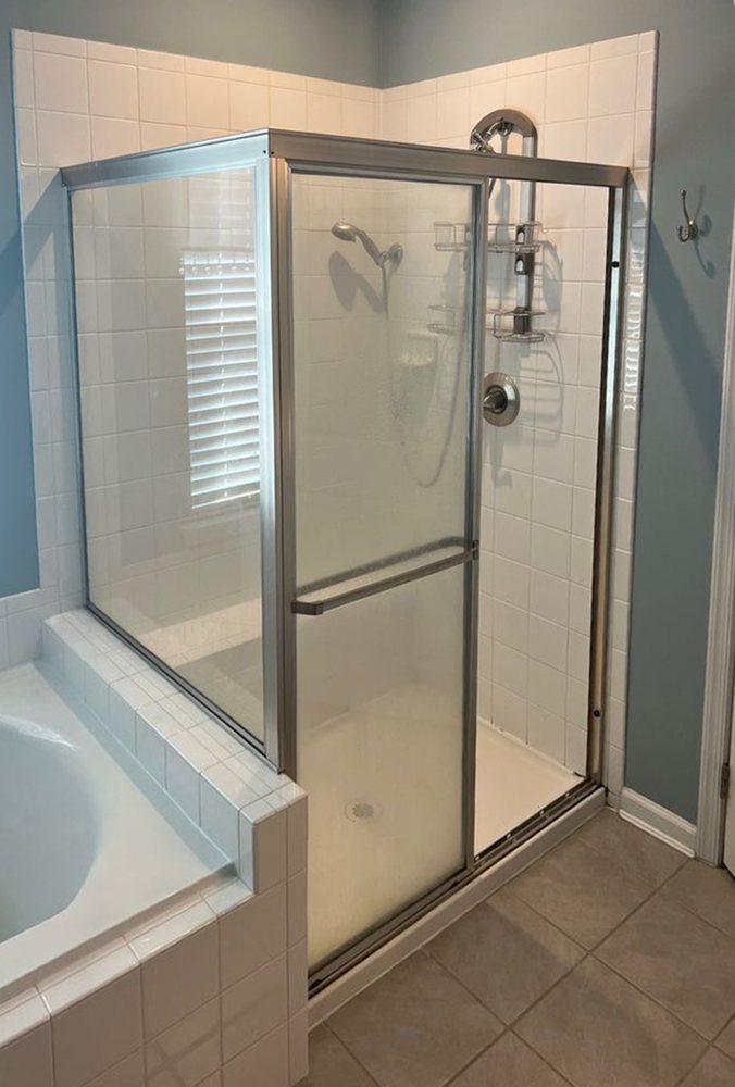Old framed shower door and panel with metal tracks, before replacement