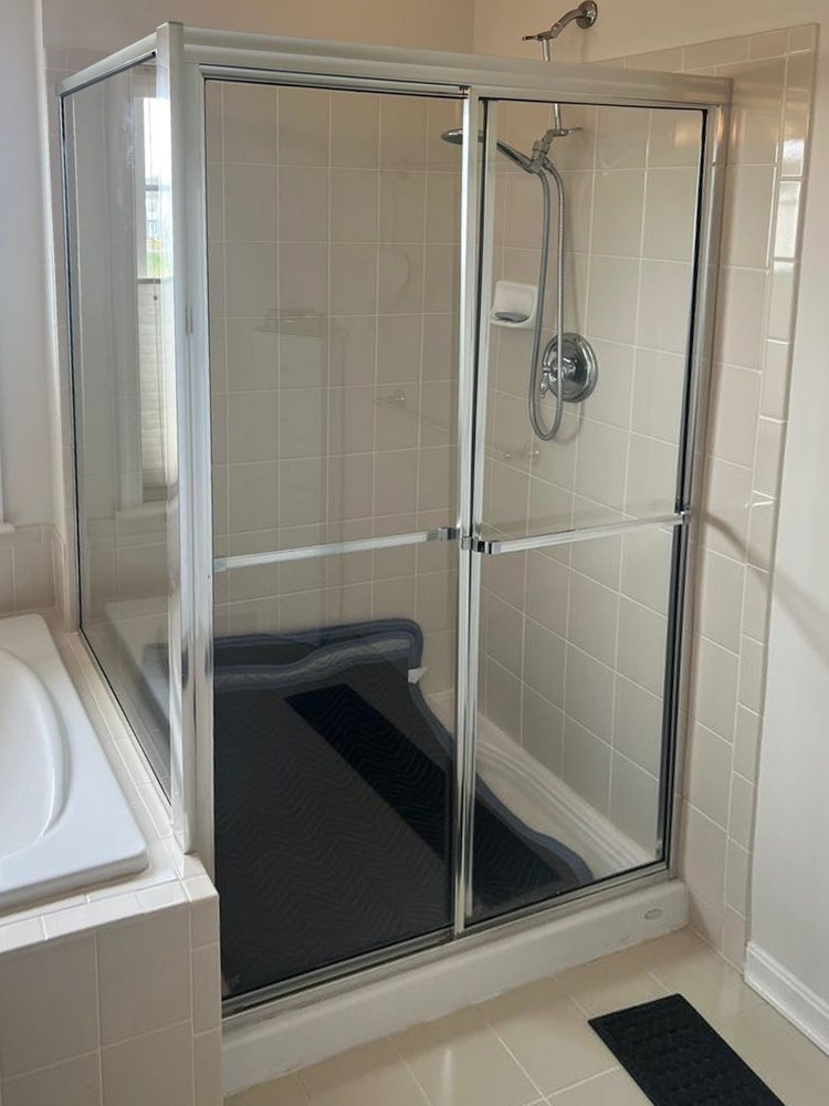 Framed shower door with a metal frame beside a soaking tub, before replacement