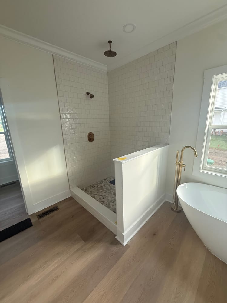 Open tiled shower with a white knee wall and brass fixtures, before the glass went in