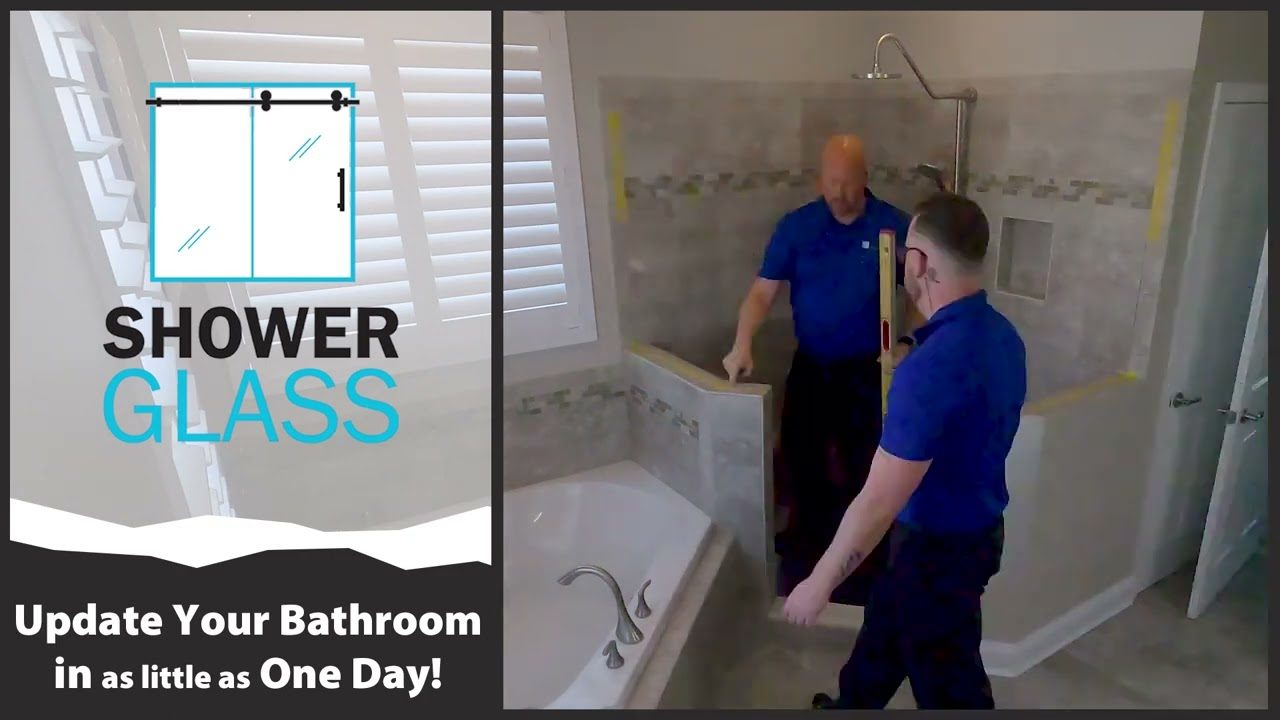 Two Shower Glass installers setting a frameless glass panel on a tiled knee wall