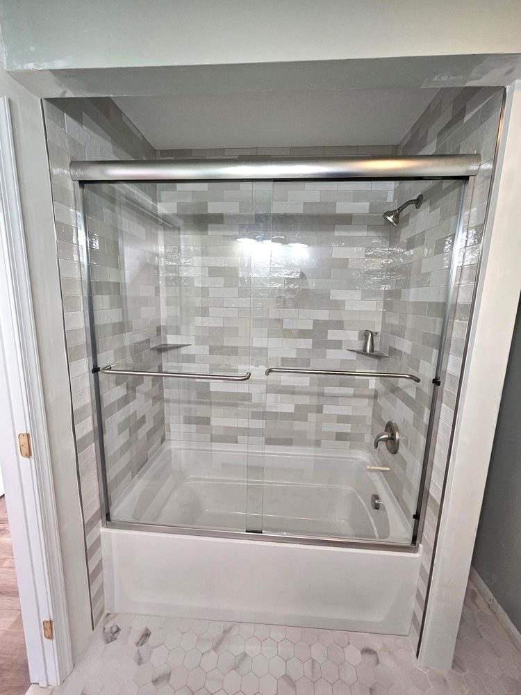 Sliding glass doors over a bathtub with brushed nickel towel bars and a top rail