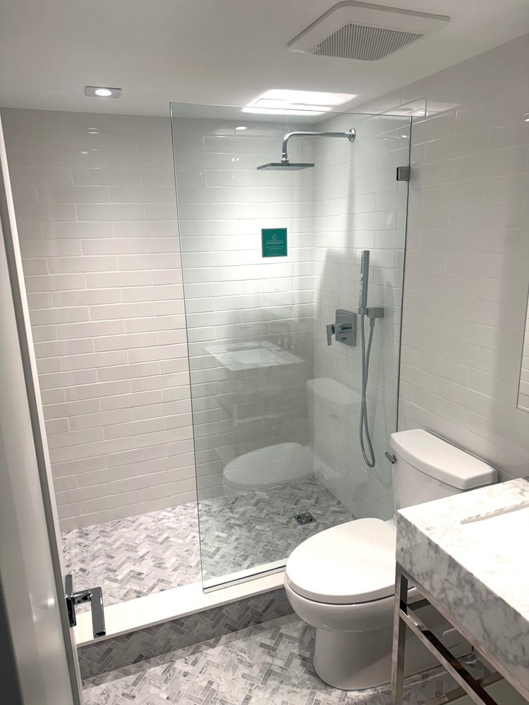 Walk-in shower with a single fixed frameless glass panel and a herringbone marble floor